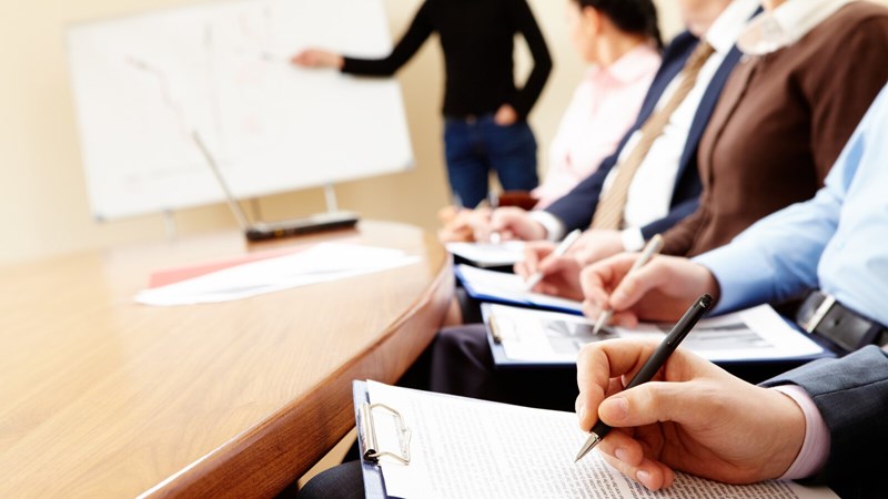 Businesspeople at a table learning from instructor near chalkboard