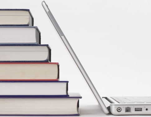 6 books stacked in a stair step pattern next to an open laptop computer with top matching angle of books