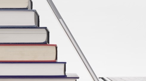6 books stacked in a stair step pattern next to an open laptop computer with top matching angle of books