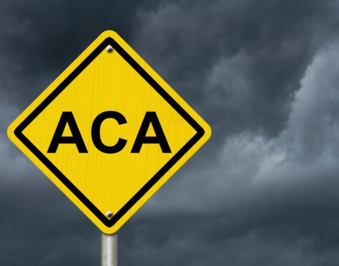 Yellow diamond warning traffic sign that says ACA with a dark cloudy sky in the background
