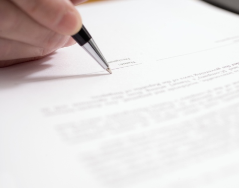 A hand holding a black pen and getting ready to sign on a signature line of a legal document