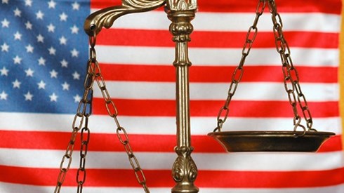Golden scales of justice in front of an American flag with yellow fringe