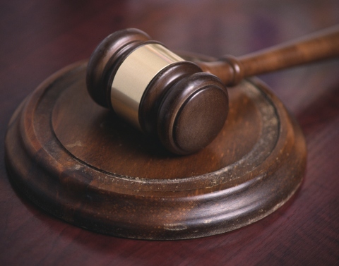 A dark brown wooden gavel with a gold band around the middle resting on a worn wooden banging disc on a wood desk