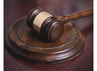 A dark brown wooden gavel with a gold band around the middle resting on a worn wooden banging disc on a wood desk