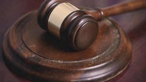 A dark brown wooden gavel with a gold band around the middle resting on a worn wooden banging disc on a wood desk