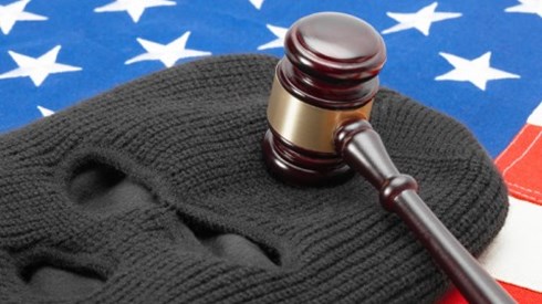 Lying on an American flag is a grey ski mask with a gavel lying on the forehead part of the mask.