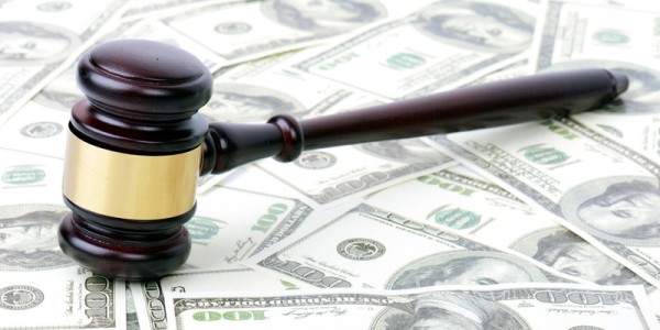 Dark brown gavel with a gold band around it resting on one hundred dollar bills that are spread out