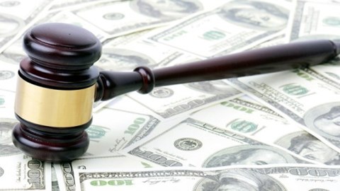 Dark brown gavel with a gold band around it resting on one hundred dollar bills that are spread out