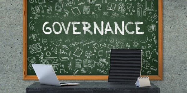 A desk with a calendar and laptop in front of a chalkboard with the word GOVERNANCE and different learning tools drawn on it
