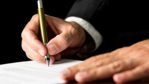 A businessman is using one hand to support a document and the other to sign it.