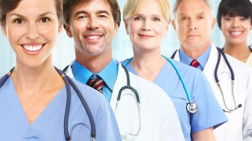 Group photo of doctors and nurses in scrubs and white coats standing behind one another