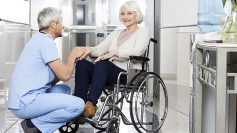 Older woman in wheelchair being greeted by a kneeling male nurse