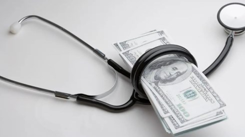 A blackstethoscope wrapped around a small stack of one-hundred-dollar bills.