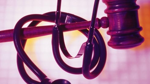 A wooden gavel with a stethoscope wrapped around it and an abstract pink and white grid background
