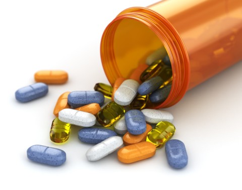 Orange pill bottle laying on it's side with many colorful pills and capsules spilling onto a white counter