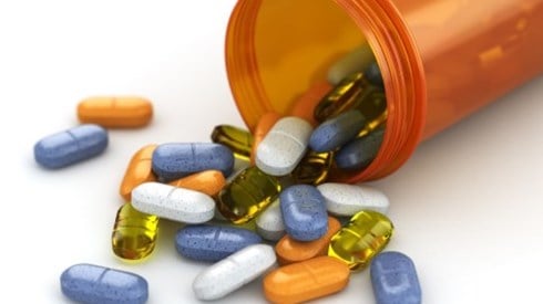 Orange pill bottle laying on it's side with many colorful pills and capsules spilling onto a white counter