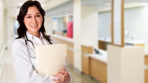 Woman medical professional with stethoscope around her neck and patient records in her arms in a medical hallway setting