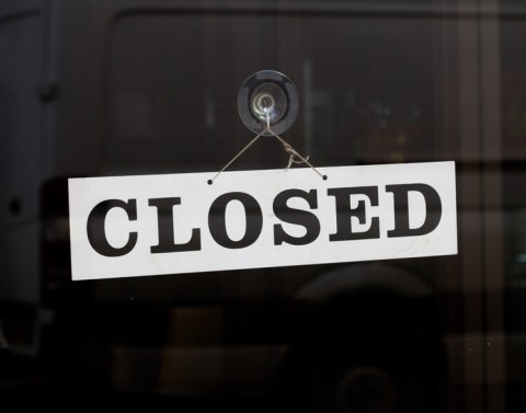A white sign reading "closed" hanging on a glass door.