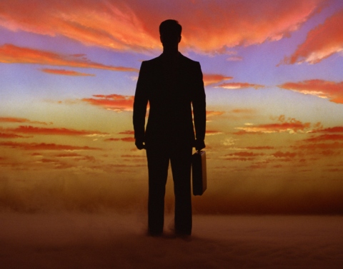 Silhouette of businessman standing against cloudy sunset