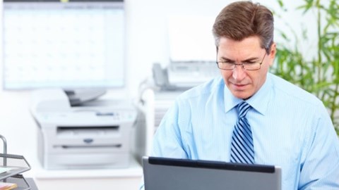 Businessman using laptop computer with office equipment blurred in the background