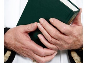 A church leader with a green book in his hands. Only his hands and torso are showing.