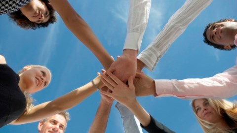A group of people in a circle extending one arm and placing their hands on top of each in the middle