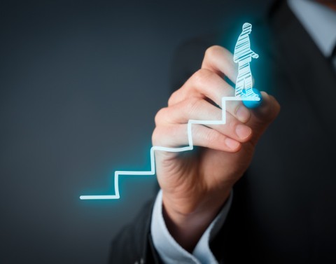 A businessman uses a blue highlighter to draw a stairwell upward with another businessman on the top step