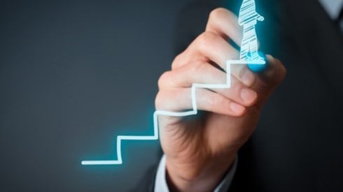 A businessman uses a blue highlighter to draw a stairwell upward with another businessman on the top step