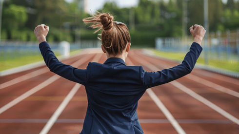 Businesswoman in a dark blue suit winning a race on a track and holding her hands up in victory
