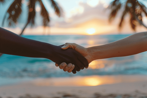 Two people shaking hands in front of a beach at sunrise