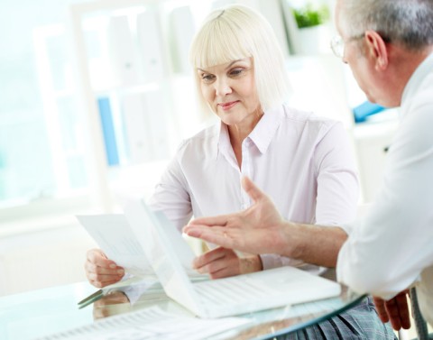 Mature businesswoman looking at document while man speaks to her