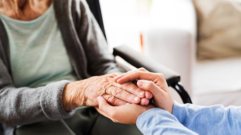 An elderly woman sitting in a chair with her hand held gently by two hands