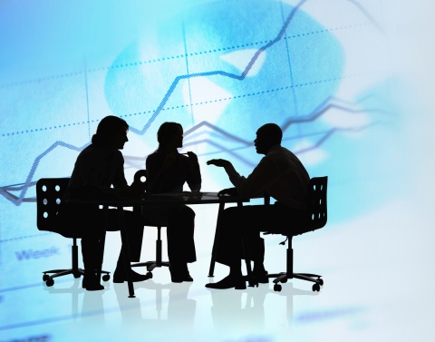 Silhouette of several people outlined in black in a meeting around a table with charts and graphs in the background