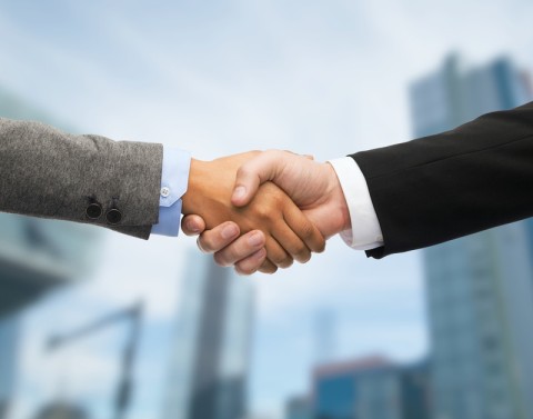 Two businessmen shaking hands with blurred skyscrapers in the background