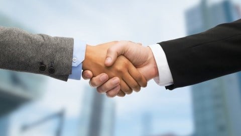 Two businessmen shaking hands with blurred skyscrapers in the background