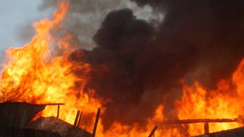 A building is being consumed by large flames of fire and black smoke.