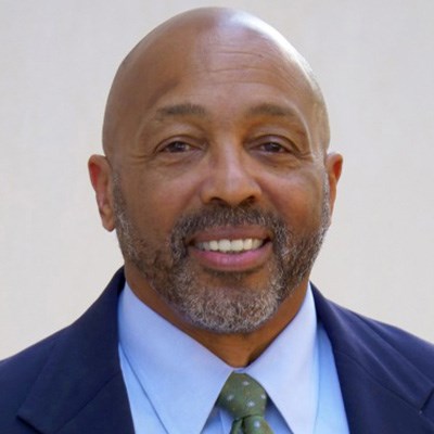 Headshot of John Talley in a navy blue suit and green tie