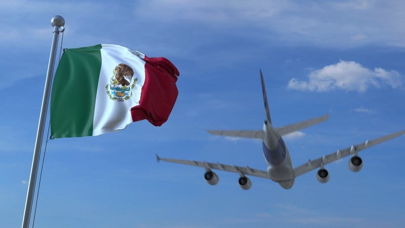 A plane landing in the background with the Mexican flag in the foreground