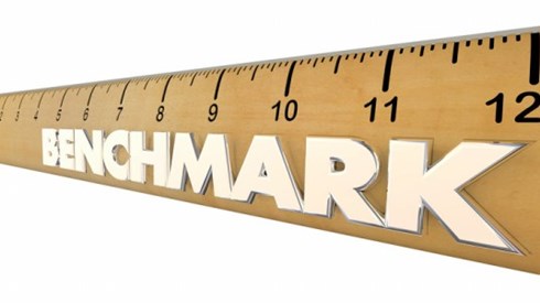 A tan 12-inch ruler with black inch markers and the word BENCHMARK in white letters stretching to the end on white background
