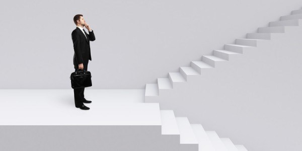 Businessman at large landing of a staircase facing the both sets of stairs and contemplating the upward set