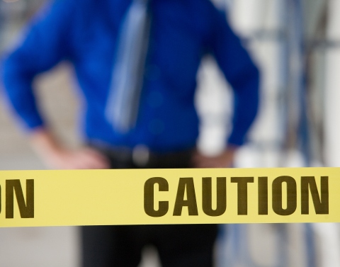 Yellow tape with the word CAUTION in black print and a man standing in the background white his hands on his hips