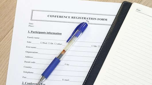 A conference registration form with a notebook and a blue pen on top of it