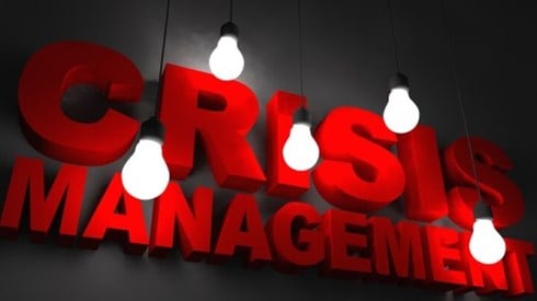 Crisis Management in Red Letters Illuminated by Hanging Lightbulbs
