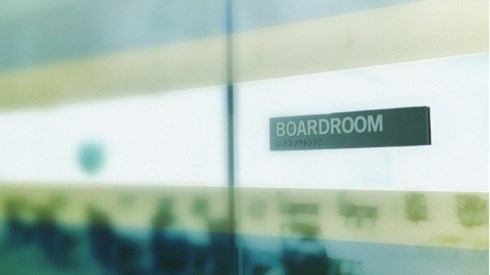 A glass conference room with the word BOARDROOM visible on the door and blurred interior of the room
