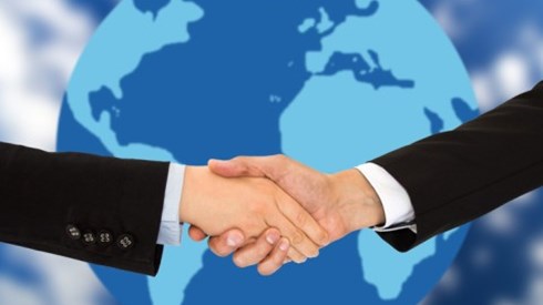 Two business professionals shake hands with a globe in the background