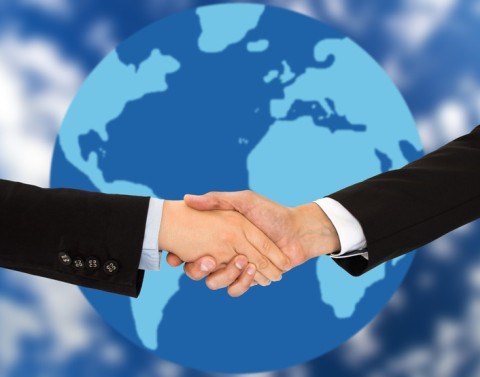 Two business professionals shake hands with a globe in the background