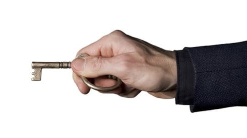 A businessman holding a skeleton key ready to insert into a lock