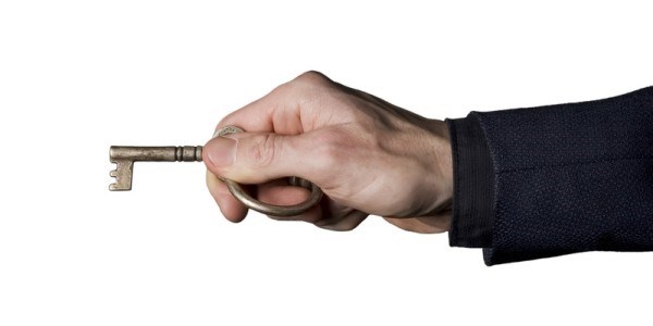A businessman holding a skeleton key ready to insert into a lock