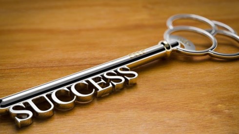 Old fashioned key with the word SUCCESS showing as the tines of the key sitting on a wood surface