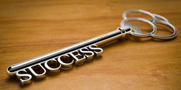 Old fashioned key with the word SUCCESS showing as the tines of the key sitting on a wood surface